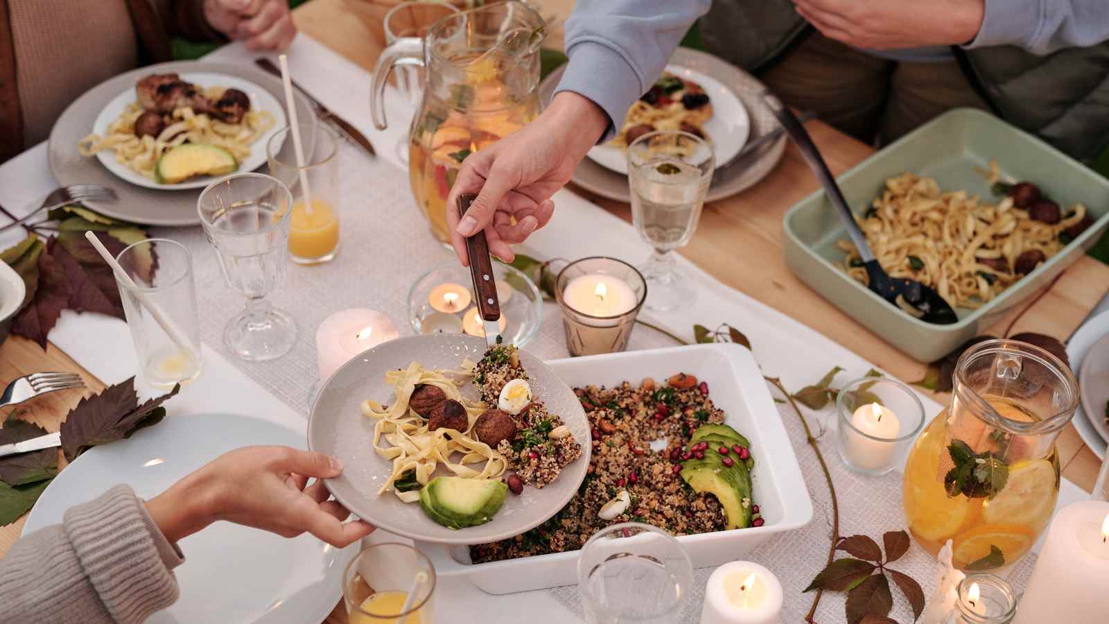 Una tavola con candele, pasta, polpette e insalata di quinoa, e le mani di chi si serve