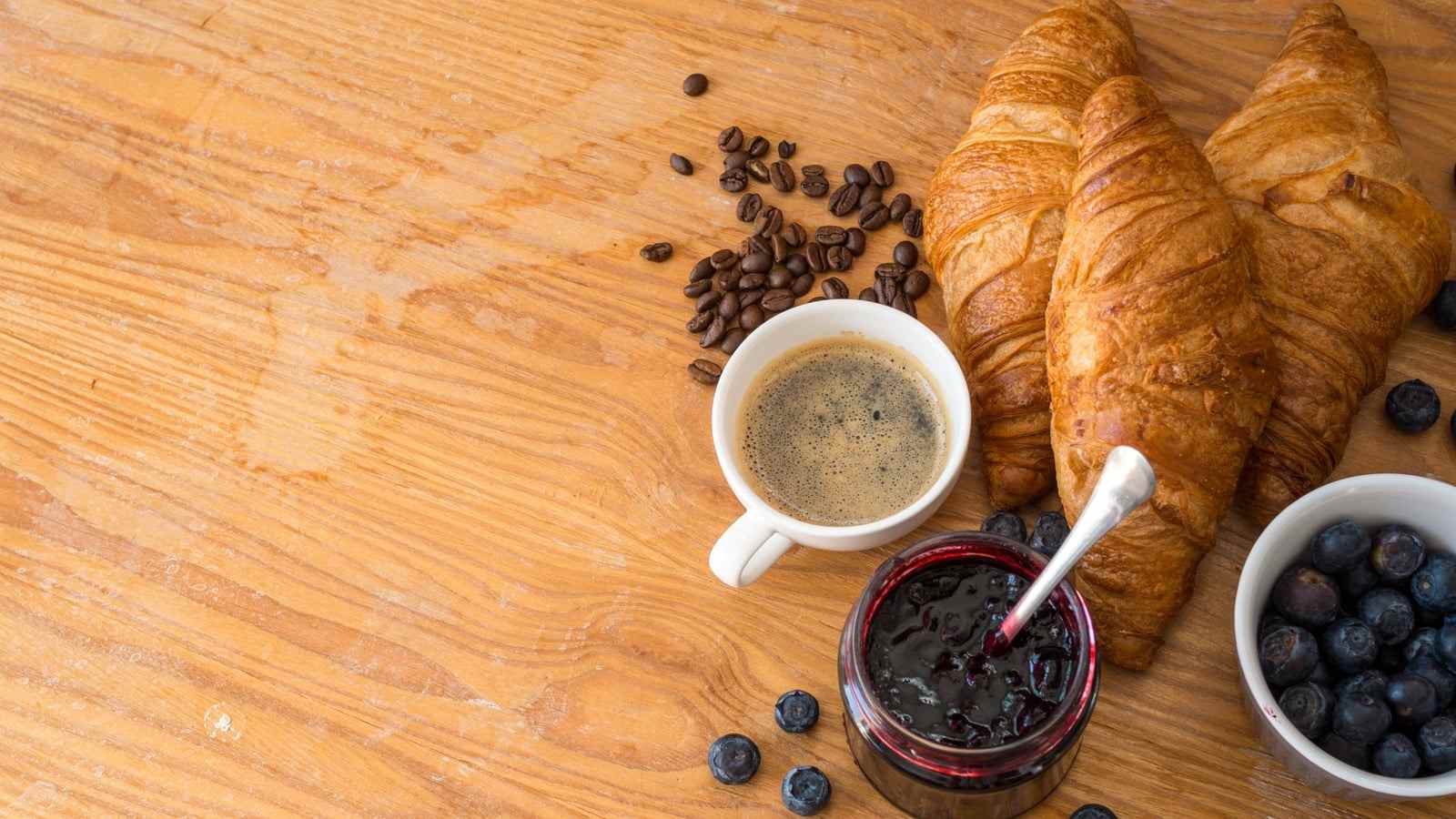 Una tazzina di caffè, cornetti, marmellata e mirtilli su un tavolo di legno
