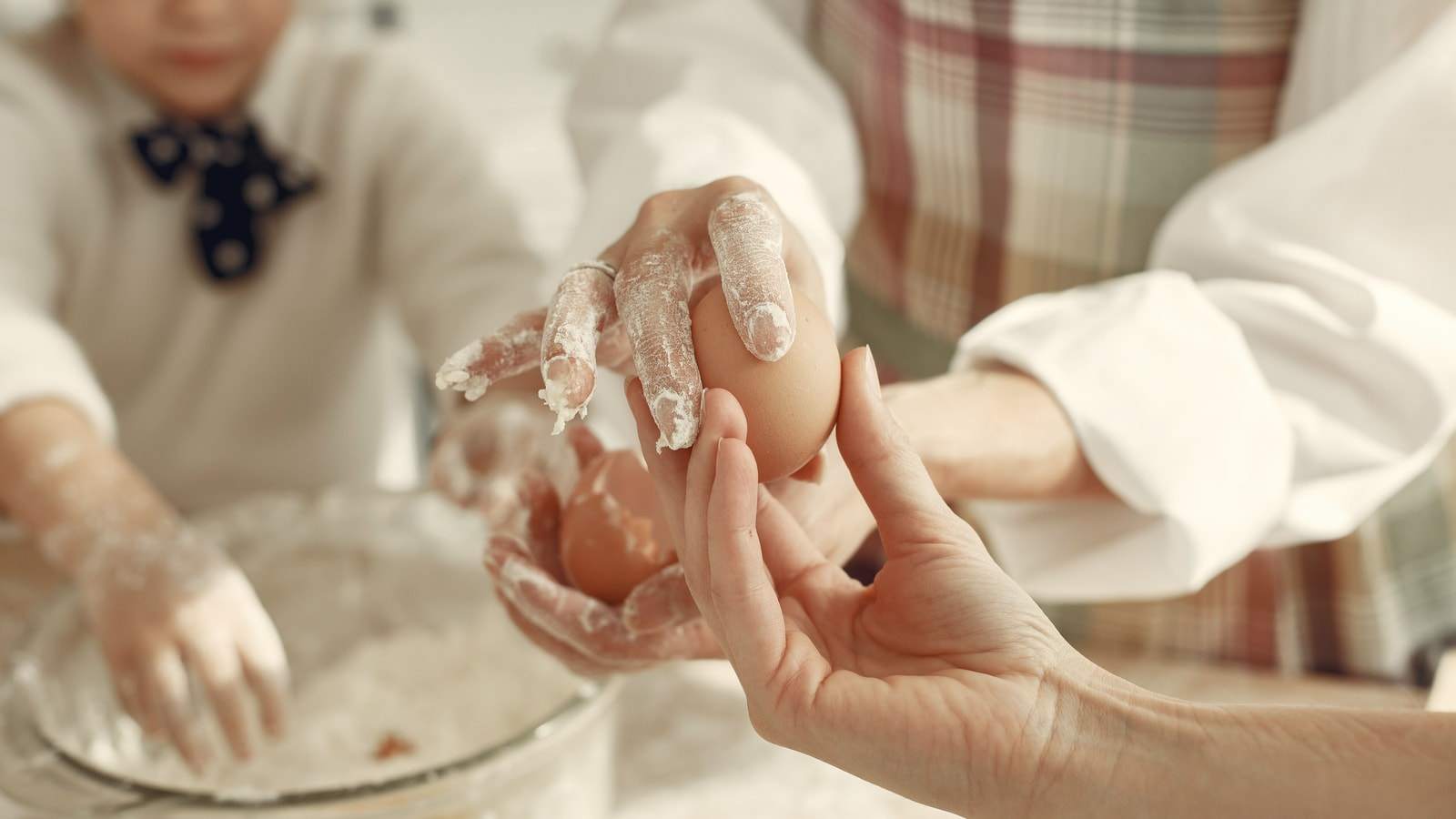 Le mani infarinate di un bambino e di un adulto preparano un impasto con le uova