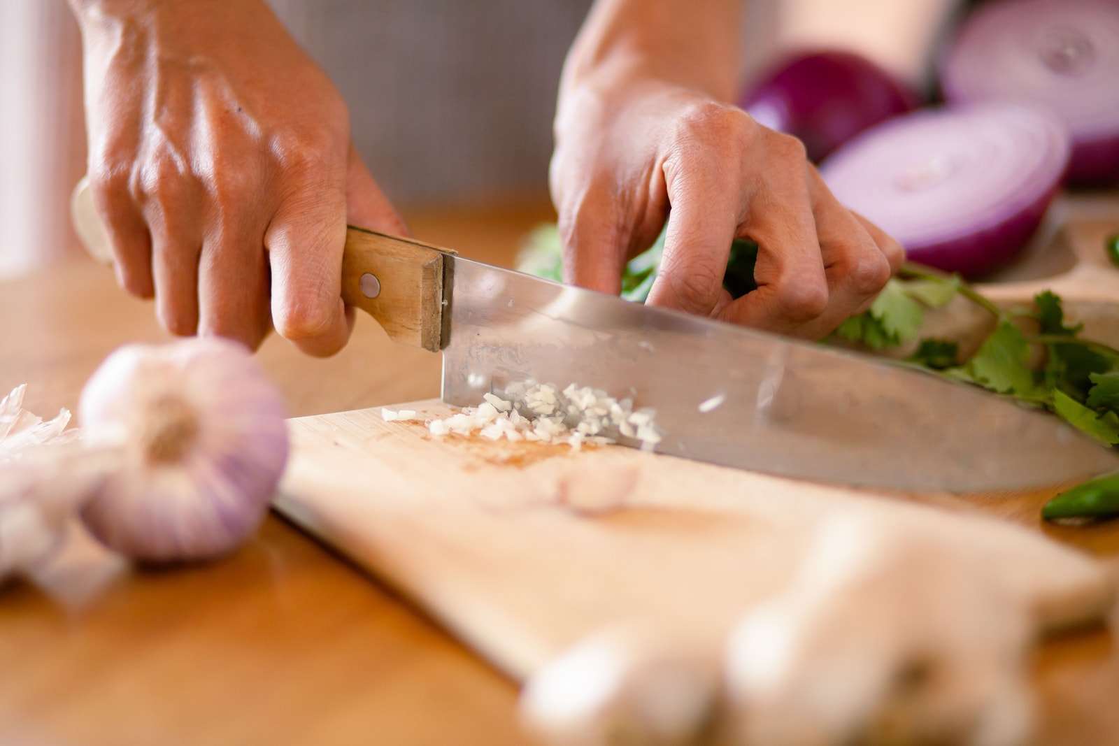 Due mani tritano l'aglio su un tagliere di legno, con due mezze cipolle rosse accanto