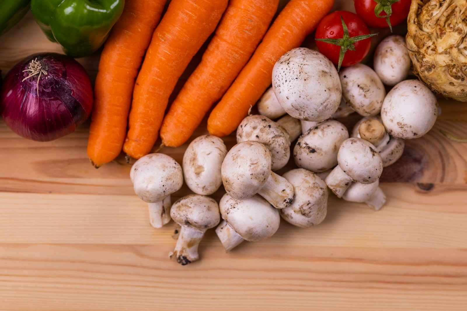 Carote, funghi, cipolla rossa, pomodori e sedano rapa su un tavolo di legno chiaro