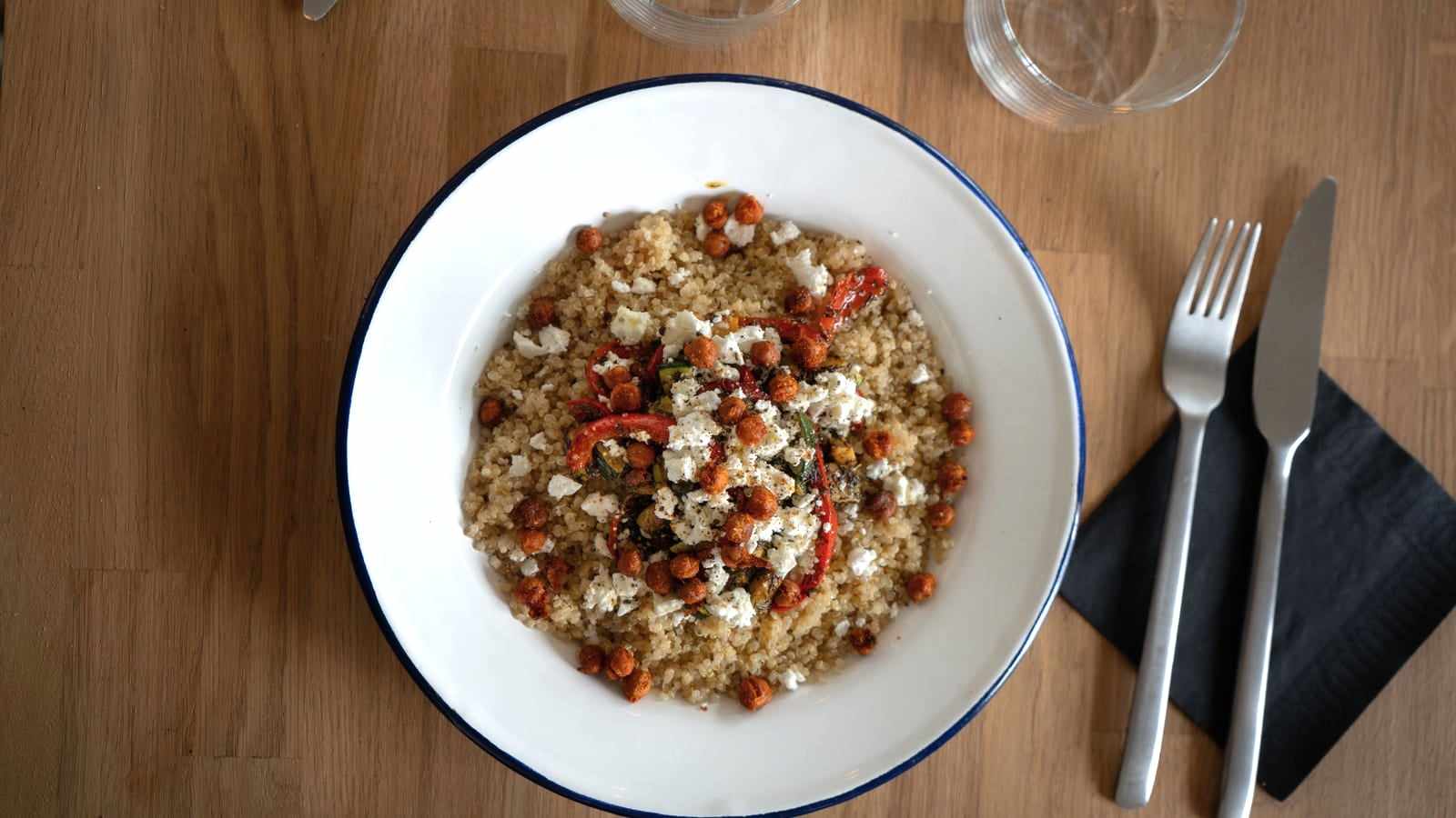 Un piatto di quinoa con ceci e peperoni, con forchetta e coltello, su un tavolo di legno