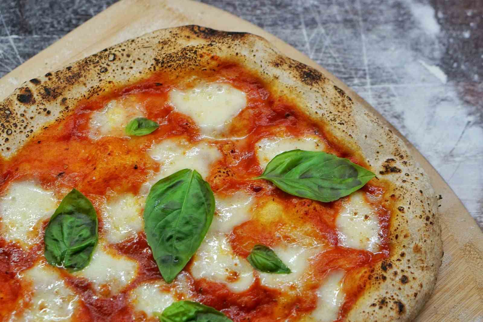 Una pizza margherita con mozzarella e basilico su una pala di legno