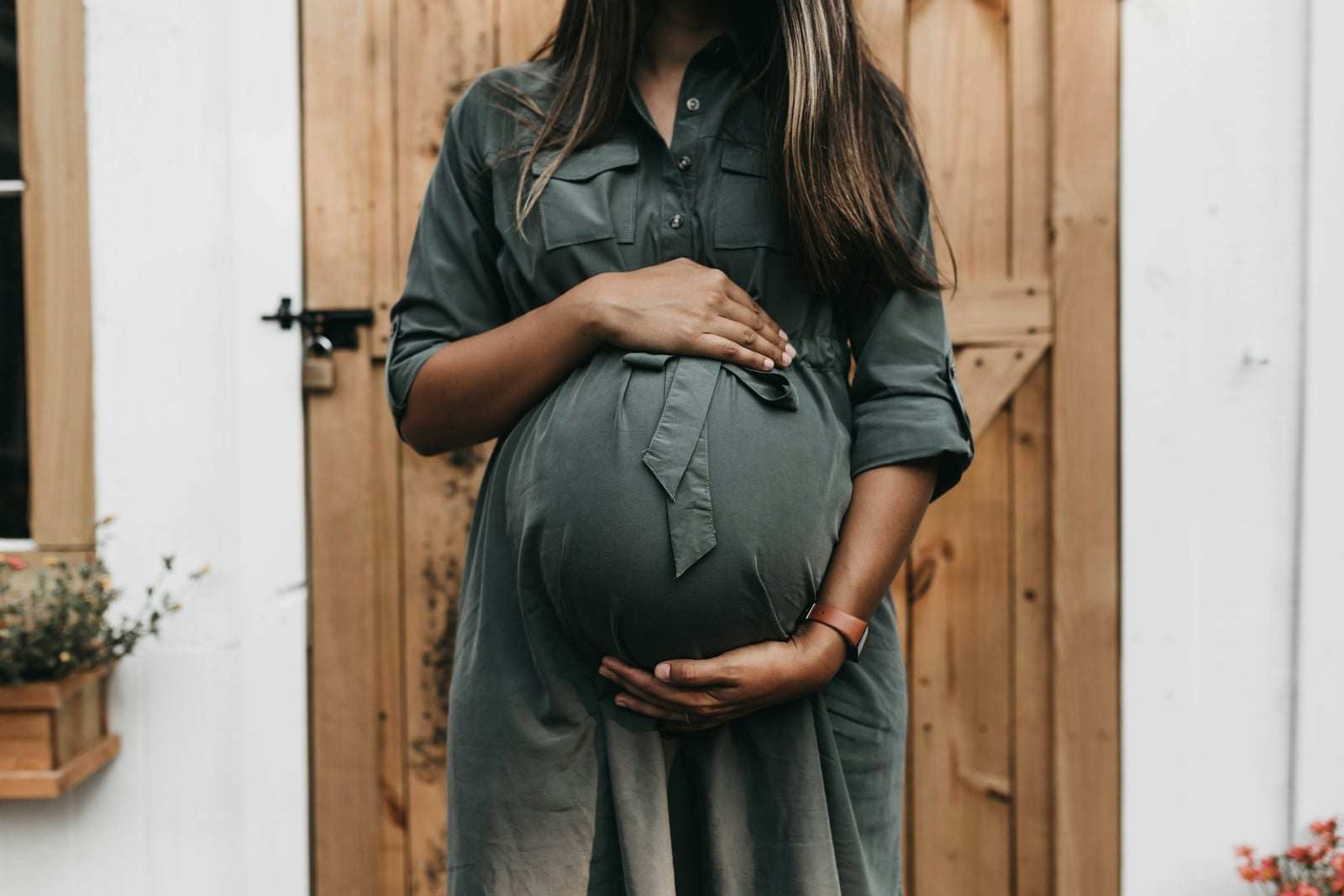 Una donna incinta in abito verde, con le mani sul ventre, davanti a una porta di legno