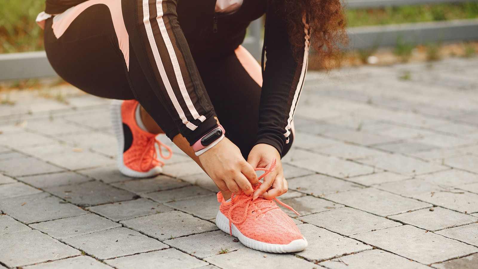 Una donna si allaccia le scarpe da corsa su un marciapiede di pietra