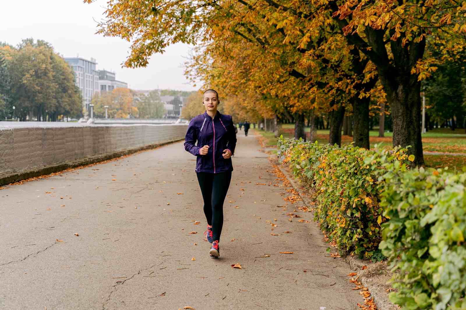 Una donna corre lungo un viale alberato in autunno, con le foglie a terra