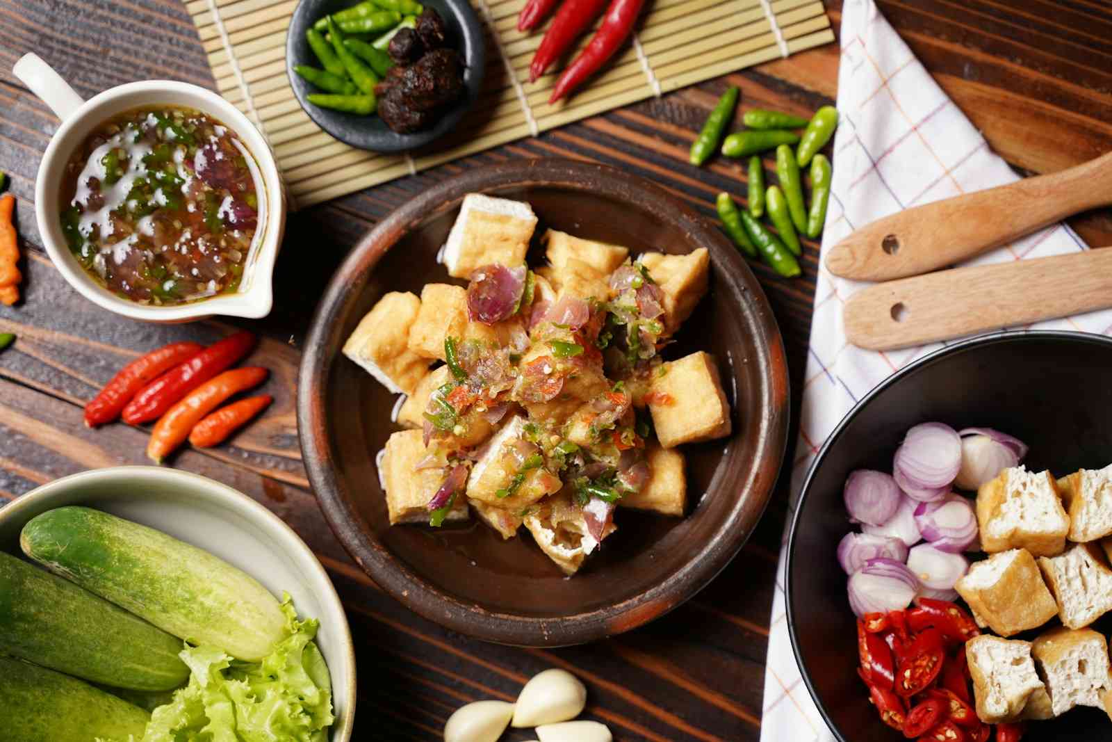 Tofu dorato in una ciotola di terracotta, con cetrioli, insalata, scalogni e peperoncini attorno