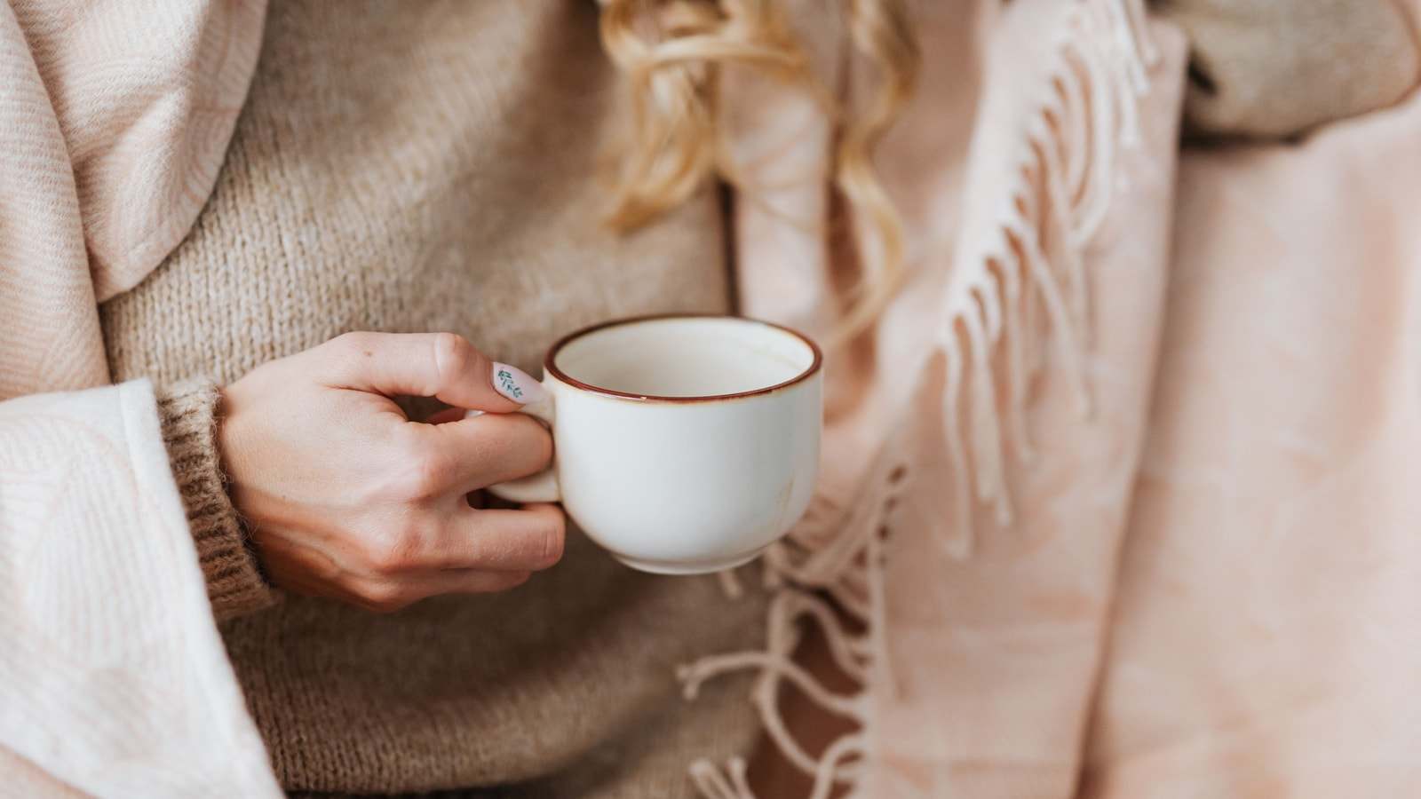 Una tazza tenuta in mano da una persona avvolta in una coperta rosa chiaro con le frange