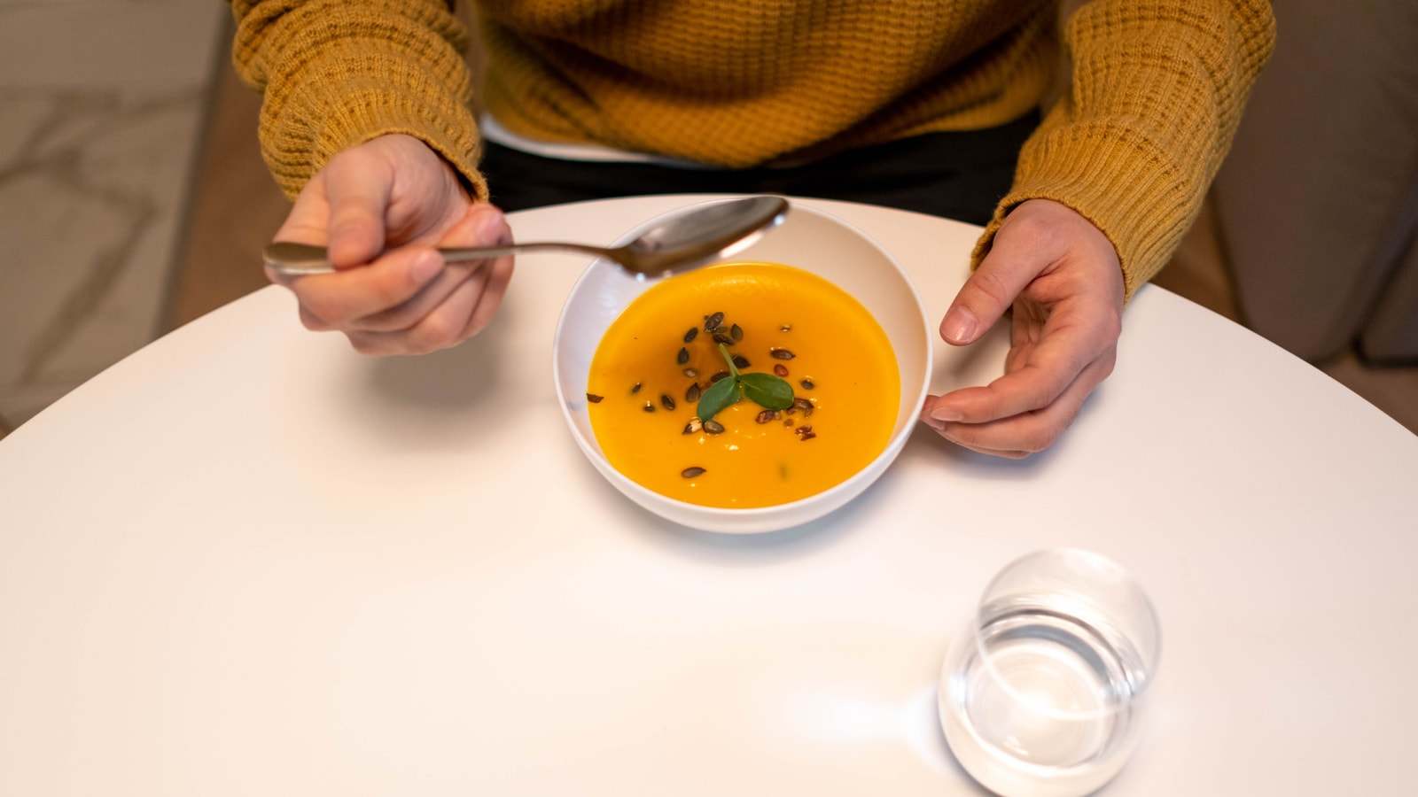 Una persona mangia una vellutata di zucca con il cucchiaio, a un tavolo bianco